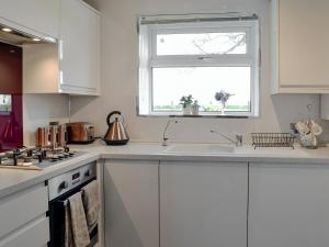 cocina blanca con fregadero y ventana en Honeysuckle Cottage, en Springside
