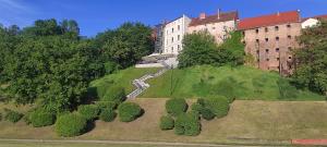 a building on top of a green hill with trees at City Center Apartment 45m, 1 Bedroom and 1 Living Room with Kitchen plus Bathroom, a perfect Family Friendly Place or for Home Office and a longer Stay, a proper office desk with business chair provided, 100m from Market Square and Vistula River in Grudziądz