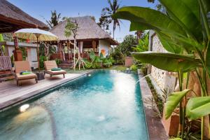 a pool in front of a house with chairs and an umbrella at Ubud Luwih Nature Retreat in Ubud