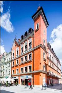 um grande edifício laranja com uma torre de relógio numa rua em Palazzo Rosso Old Town em Poznań