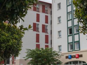 un edificio alto de color blanco con ventanas de contraventanas rojas en ibis budget Ciboure St-Jean-Luz, en Ciboure