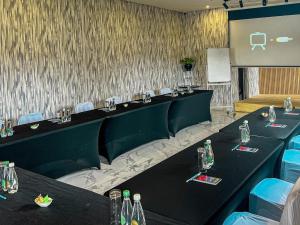 Monte La Vue Hotel في Sandton: قاعة اجتماعات بها طاولات سوداء وكراسي وشاشة