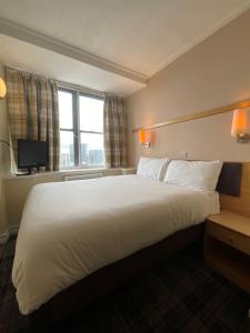 ein großes weißes Bett in einem Hotelzimmer mit Fenster in der Unterkunft Britannia Inn Glasgow in Glasgow