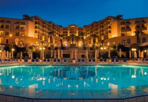 a swimming pool in front of a hotel at night at Corinthia St George's Bay in St. Julianʼs
