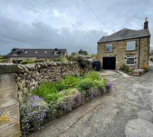 a stone house with a stone wall and flowers at Burnside Cottage, Wark, Hexham in Hexham