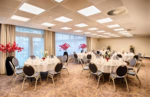 ハンブルクにあるレオナルド ホテル ハンブルク シティ ノードの白いテーブルと椅子、赤い花が飾られた宴会場