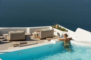 a woman standing in a swimming pool next to the ocean at Canaves Ena - Small Luxury Hotels of the World in Oia