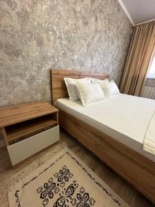 Schlafzimmer mit einem Bett mit einem Kopfteil aus Holz und einem Tisch in der Unterkunft Уютная квартира недалеко от Аэропорта in Qostanai