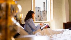 a woman sitting on a bed reading a magazine at Palazzo Zacà in Gallipoli
