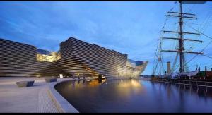 a large building next to a river with a boat at Easy sleep in Dundee