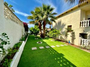une cour avec de l'herbe verte et des palmiers à côté d'un bâtiment dans l'établissement Karma Villa with views by HLCLUB Agency, à Sant Pere de Ribes