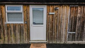 un edificio de madera con puerta blanca y 2 ventanas en Wild Valley Huts, en Llanrhaeadr-ym-Mochnant
