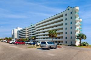 un grand bâtiment blanc avec des voitures garées dans un parking dans l'établissement Plantation Palms 6408, à Gulf Highlands