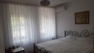 サラエボにあるApartmani Zaaraのベッドルーム1室(ベッド1台付)、白いカーテン付きの窓2つが備わります。