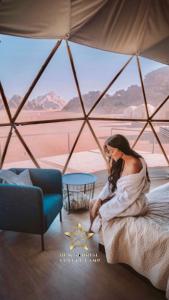 une femme assise sur un lit dans une pièce avec vue dans l'établissement RUM SUNRlSE LUXURY CAMP, à Wadi Rum