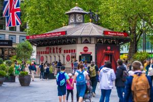 a group of people walking in front of a kiosk at Central quality point piccadilly in London