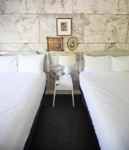 two beds with white sheets and a table with a lamp at The Briarcliff Motel in Great Barrington