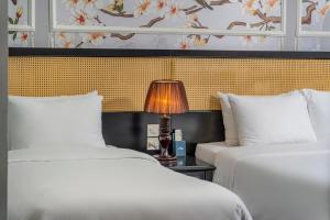 two beds in a room with a lamp on a table at Amara Hanoi Hotel and Spa in Hanoi