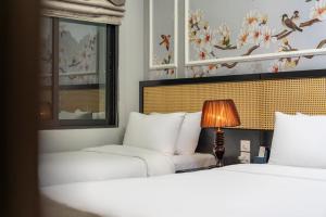 a bedroom with two beds and a lamp and a window at Amara Hanoi Hotel and Spa in Hanoi
