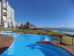 a large swimming pool with a view of the ocean at Coastal Hospitality - Beach Club 401 in Mossel Bay