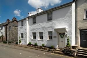 a white house with a green door on a street at Wharton Cottage, Lake District Retreat in Cartmel