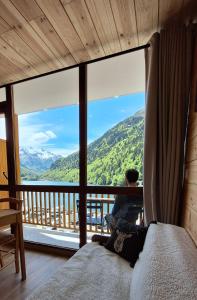 a man sitting on a bed in a room with a large window at Appartement chaleureux en cœur de station in Laruns