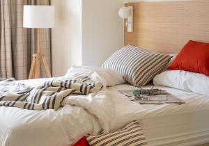 uma cama com lençóis e almofadas brancos e um candeeiro em Apartahotel Líbere Vitoria em Vitoria-Gasteiz