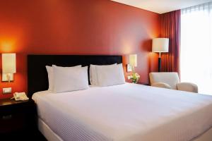 um quarto com uma grande cama branca com paredes vermelhas em NH Puebla Centro Histórico em Puebla