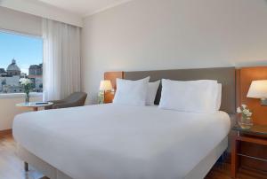 uma grande cama branca num quarto de hotel com uma janela em NH Montevideo Columbia em Montevidéu