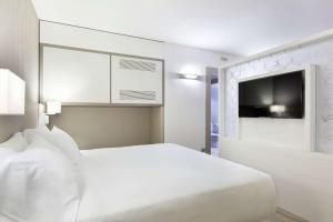 a white bedroom with a bed and a flat screen tv at NH Milano Congress Centre in Assago