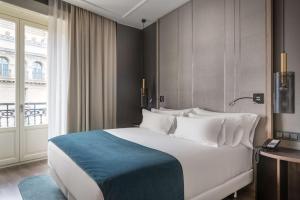 a large white bed in a room with a window at NH Collection Madrid Gran Vía in Madrid