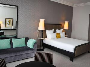 カブールにあるLe Grand Hotel de Cabourg - MGallery Hotel Collectionのベッドとソファ付きのホテルルーム