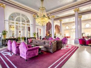 a living room with purple furniture and a chandelier at Le Grand Hotel de Cabourg - MGallery Hotel Collection in Cabourg