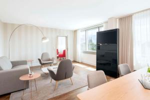 een woonkamer met een bank en stoelen en een tv bij NH Collection Köln Mediapark in Keulen