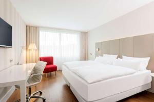 una habitación de hotel con una gran cama blanca y una silla roja en NH Collection Köln Mediapark en Colonia