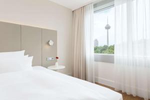 een witte slaapkamer met een groot bed en een raam bij NH Collection Köln Mediapark in Keulen