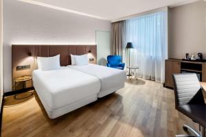 NH Luxembourg في لوكسمبورغ: غرفة فندق بسرير ابيض كبير وكرسي ازرق