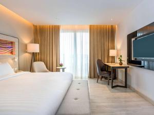 a hotel room with a bed and a desk and a television at Novotel Phuket City Phokeethra in Phuket Town