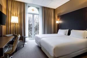 a hotel room with two beds and a desk and a window at NH Centre Utrecht Hotel in Utrecht