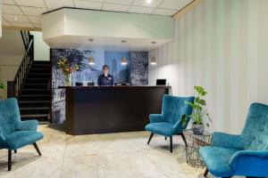 a man standing at a counter in a lobby with blue chairs at NH Centre Utrecht Hotel in Utrecht