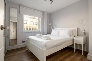 een witte slaapkamer met een wit bed en een raam bij GuestReady - Central Living near Kensington Palace in Londen