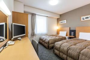 a hotel room with two beds and a desk with a television at Comfort Hotel Kushiro in Kushiro