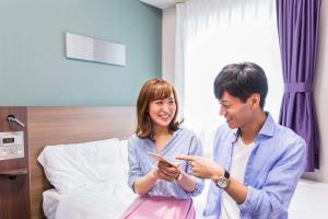 Un uomo e una donna che guardano un cellulare di Comfort Hotel Kushiro a Kushiro