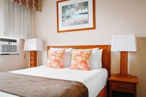a bedroom with a bed with pillows and two lamps at Banyan Harbor Resort in Lihue