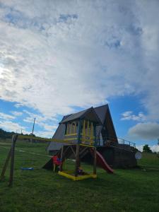 een speeltuin met een huis en een glijbaan in een veld bij Under Sky House - Vikendica - Manjača in Ključ