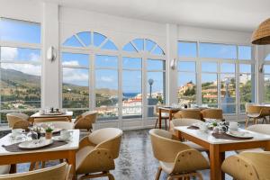 restauracja ze stołami i krzesłami oraz dużymi oknami w obiekcie Paradise Art Hotel w mieście Andros