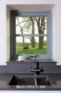a kitchen sink with a window with a dog outside at Discovery - Luxury Cosy Country Escape in Grantham