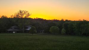 een zonsondergang boven een veld met een huis en bomen bij The Little House at EVOO in Cookeville