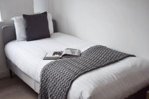 a bed with a black and white blanket and a book on it at Stylish 2BR - 1 minute walk from Elizabeth Line in Romford