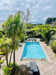a swimming pool with palm trees on a wooden deck at Villa rospico, 200m de la plage avec piscine in Névez